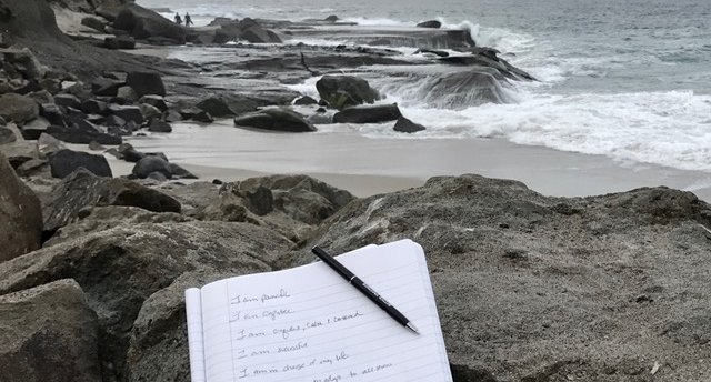 Image of notebook filled with personal mantras sitting on the rocks at the beach